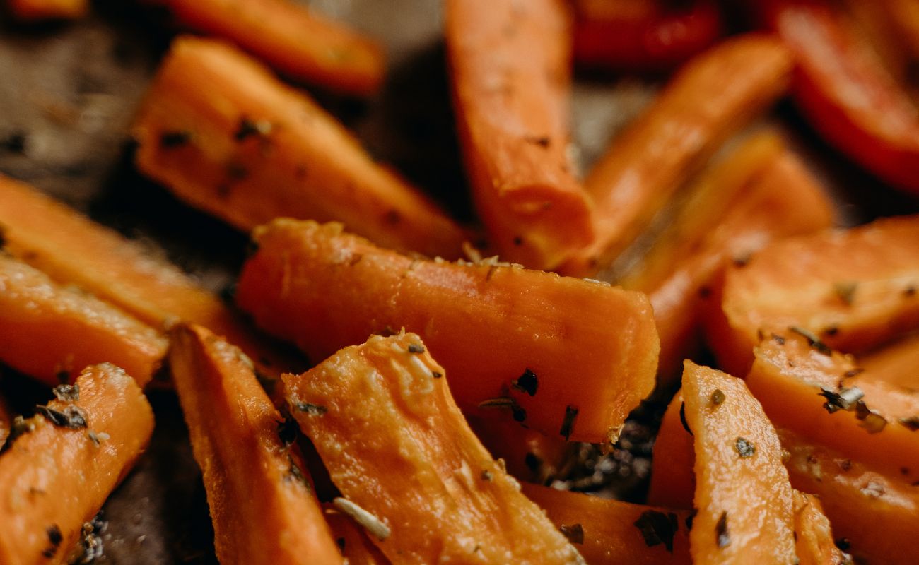 Legume la cuptor caramelizate cu miere Mānuka, servite pe platou rustic, decorate cu ierburi aromate