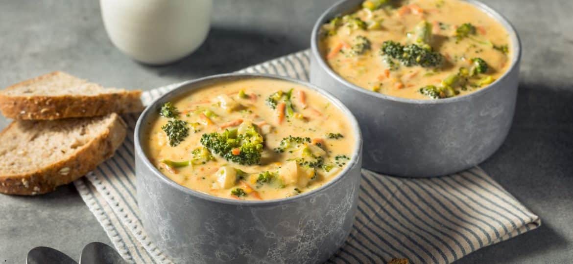 Supă cremoasă de broccoli și cheddar servită într-un bol rustic, decorată cu brânză rasă și crutoane aurii