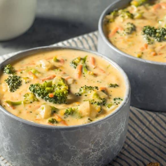 Supă cremoasă de broccoli și cheddar servită &icirc;ntr-un bol rustic, decorată cu br&acirc;nză rasă și crutoane aurii