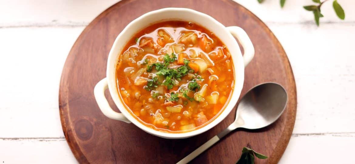 Supă de varză cu legume și fasole albă servită într-un bol rustic, decorată cu verdețuri proaspete